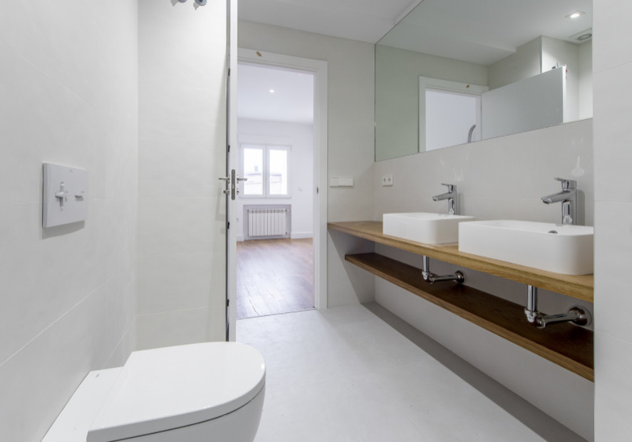 Foto på ett stort funkis brun en-suite badrum, med vita skåp, en kantlös dusch, en vägghängd toalettstol, beige kakel, beige väggar, klinkergolv i porslin, ett fristående handfat, träbänkskiva, grått golv och med dusch som är öppen