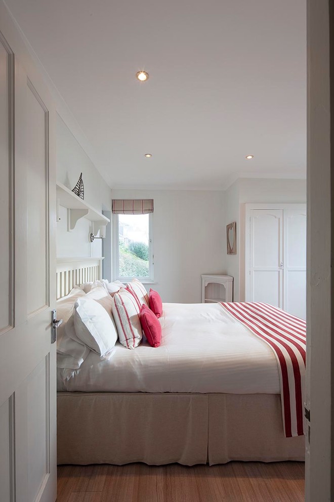 This is an example of a mid-sized beach style master bedroom in Cornwall with white walls, light hardwood floors, no fireplace and beige floor.