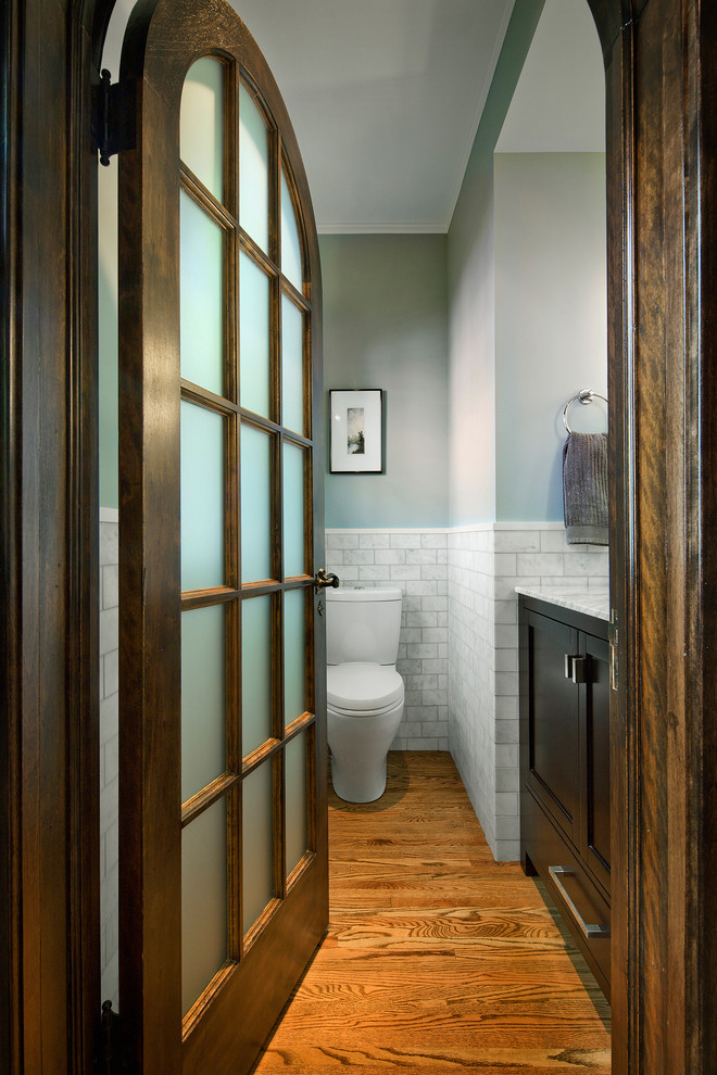 Design ideas for a mid-sized traditional 3/4 bathroom in Minneapolis with shaker cabinets, brown cabinets, a two-piece toilet, gray tile, white tile, subway tile, grey walls, medium hardwood floors, an undermount sink and marble benchtops.