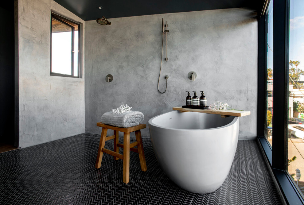 Cette photo montre une salle de bain industrielle avec une baignoire indépendante, une douche ouverte, un sol noir, un carrelage gris, un sol en carrelage de porcelaine et aucune cabine.