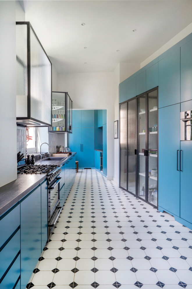 Ejemplo de cocina contemporánea con armarios tipo vitrina, puertas de armario azules, salpicadero verde, electrodomésticos negros y encimeras grises