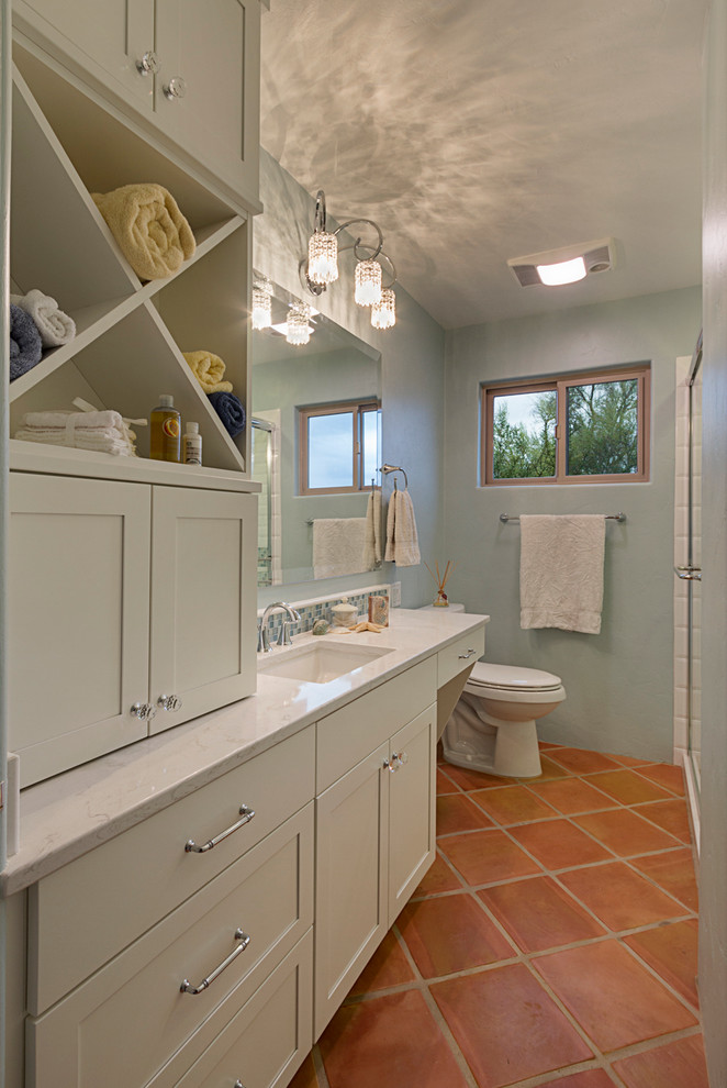 Photo of a small beach style 3/4 bathroom in Phoenix with an undermount sink, shaker cabinets, white cabinets, an alcove shower, a one-piece toilet, blue tile, subway tile, blue walls, terra-cotta floors and laminate benchtops.