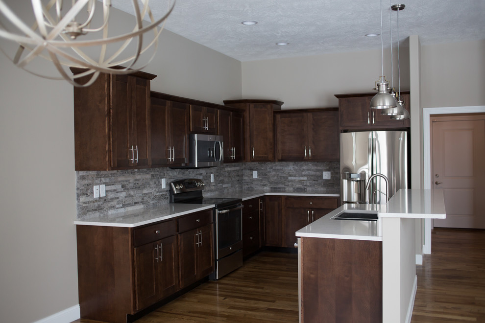 Inspiration for a mid-sized transitional l-shaped dark wood floor enclosed kitchen remodel with a double-bowl sink, shaker cabinets, dark wood cabinets, quartz countertops, gray backsplash, stone tile backsplash, stainless steel appliances and an island