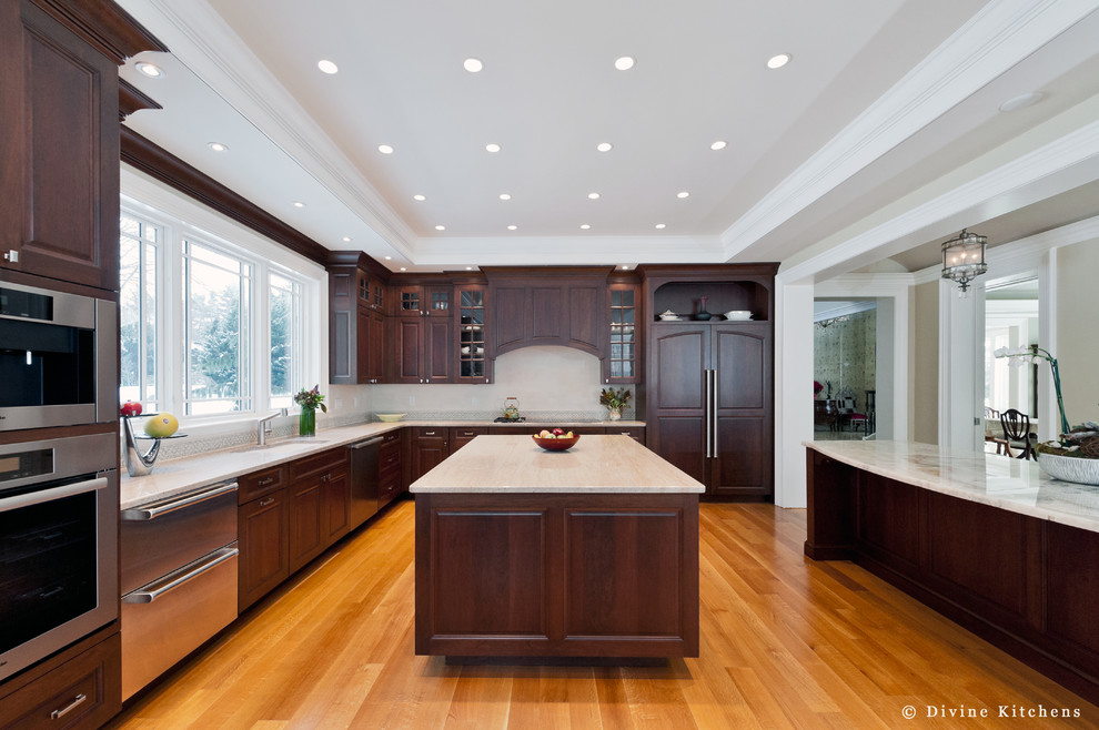Large traditional u-shaped eat-in kitchen in Boston with an undermount sink, raised-panel cabinets, dark wood cabinets, beige splashback, stainless steel appliances, light hardwood floors, multiple islands and quartzite benchtops.