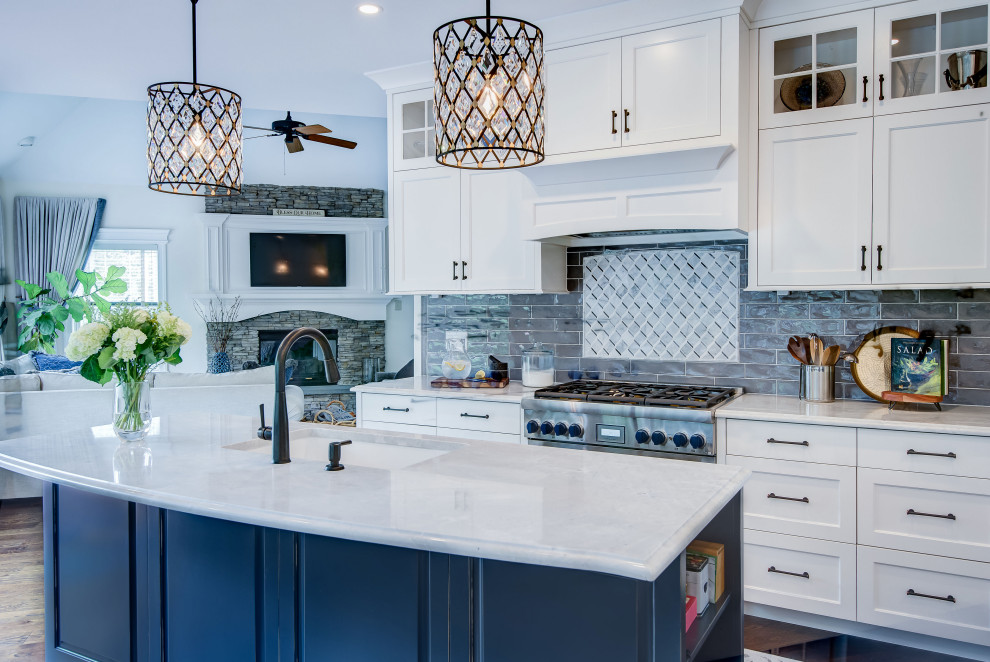 Inredning av ett klassiskt mellanstort vit vitt kök, med en undermonterad diskho, släta luckor, blå skåp, bänkskiva i kvartsit, grått stänkskydd, rostfria vitvaror, mellanmörkt trägolv, en köksö och brunt golv