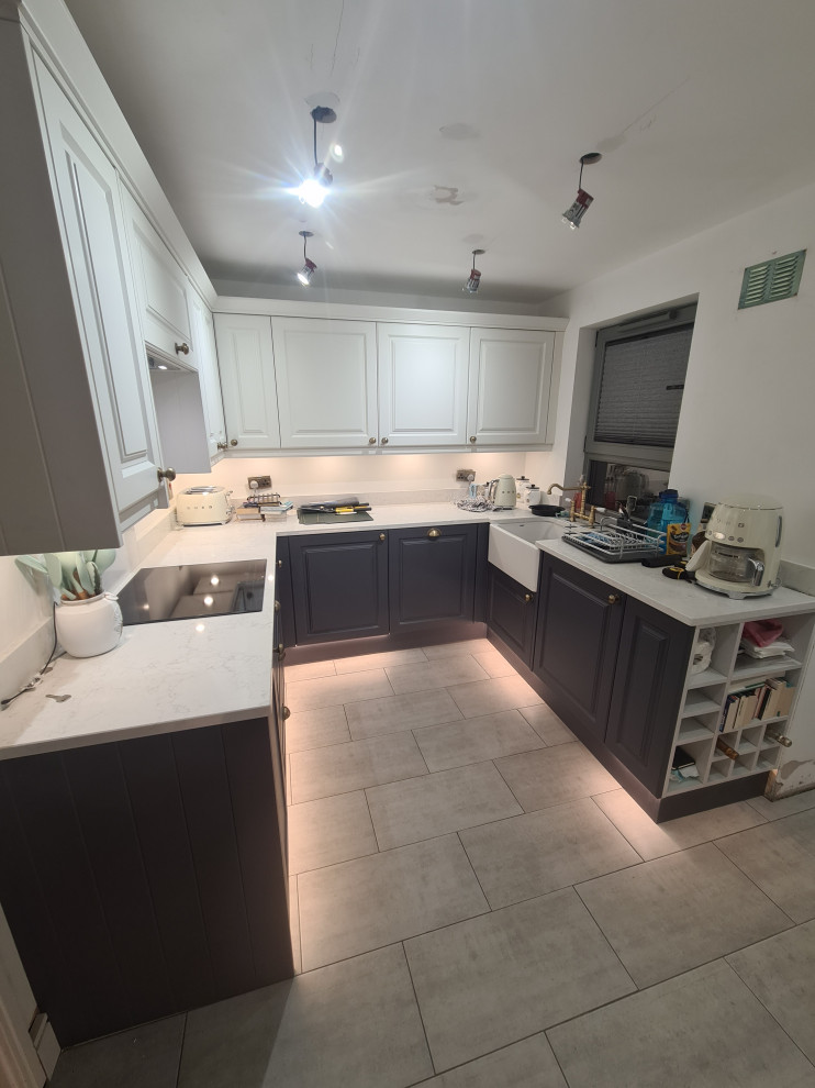 Photo of a large victorian grey and white u-shaped open plan kitchen in London with a belfast sink, shaker cabinets, white cabinets, quartz worktops, white splashback, ceramic splashback, integrated appliances, ceramic flooring, grey floors, white worktops and feature lighting.