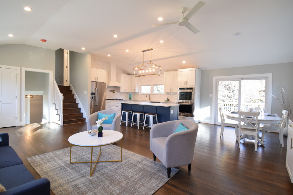 This is an example of a large transitional l-shaped eat-in kitchen in Baltimore with a farmhouse sink, shaker cabinets, white cabinets, quartz benchtops, white splashback, cement tile splashback, stainless steel appliances, dark hardwood floors, with island, brown floor and white benchtop.