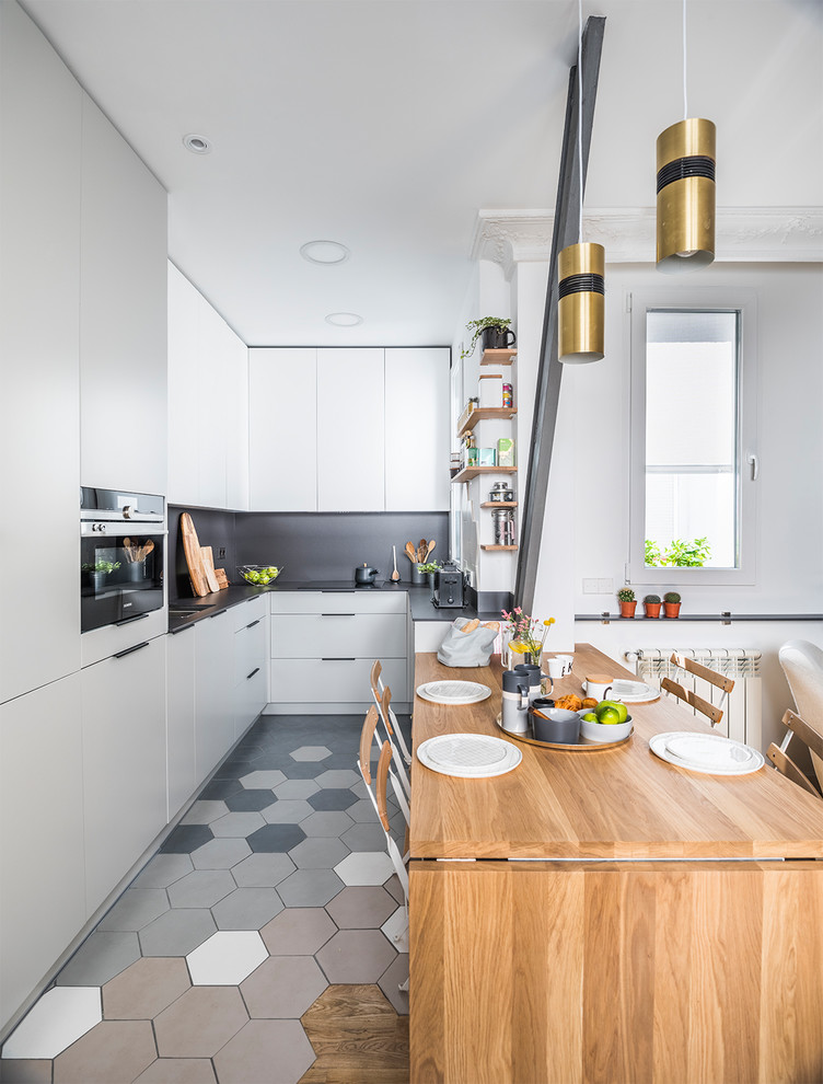 This is an example of a contemporary u-shaped open plan kitchen in Madrid with flat-panel cabinets, black splashback, black appliances, black benchtop, an undermount sink, white cabinets, a peninsula and multi-coloured floor.