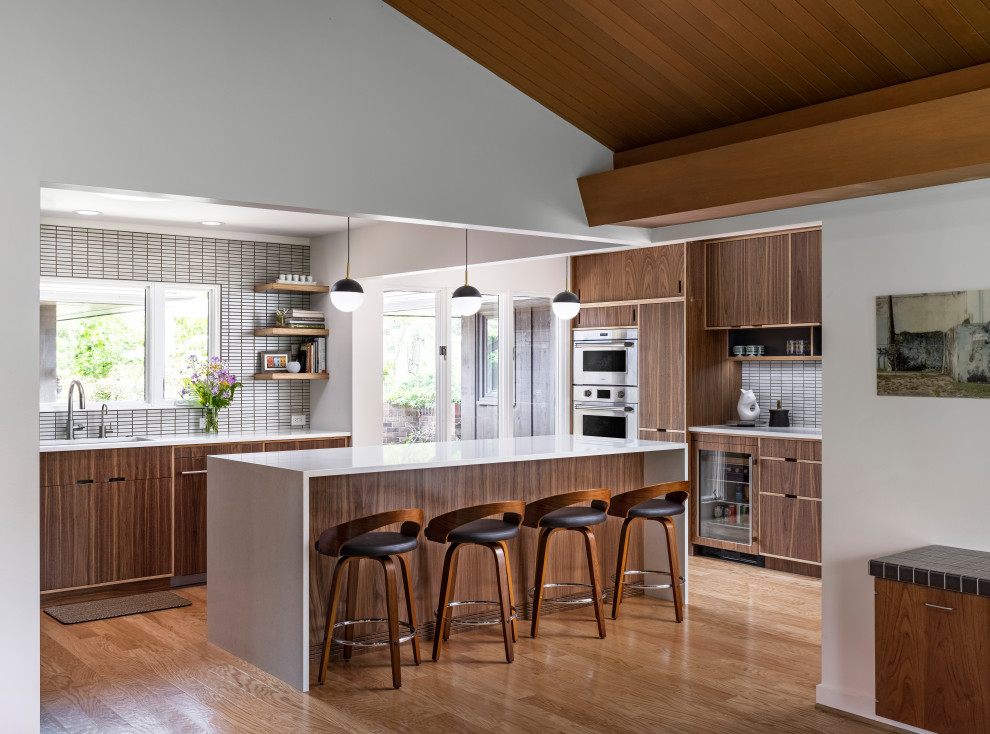 Design ideas for a midcentury galley eat-in kitchen in Detroit with white splashback, with island, white benchtop, an undermount sink, flat-panel cabinets, dark wood cabinets, quartz benchtops, mosaic tile splashback, stainless steel appliances, medium hardwood floors and wood.
