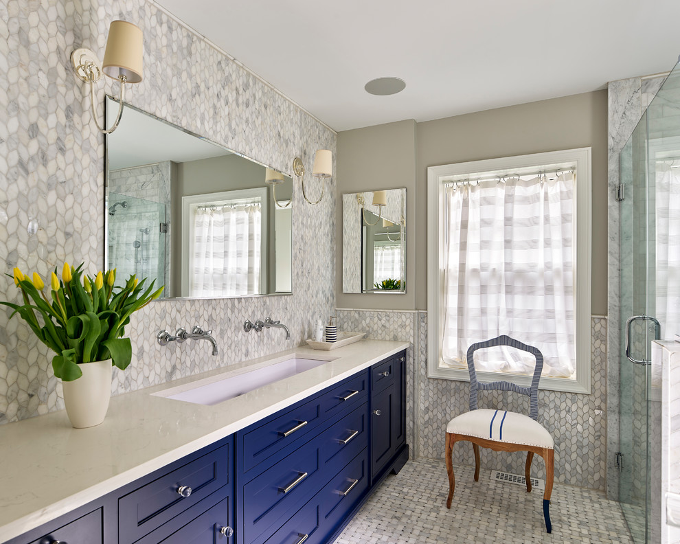 This is an example of a mid-sized transitional master bathroom in Philadelphia with blue cabinets, a curbless shower, gray tile, mosaic tile, mosaic tile floors, a trough sink, solid surface benchtops, grey floor, a hinged shower door, shaker cabinets, grey walls and beige benchtops.