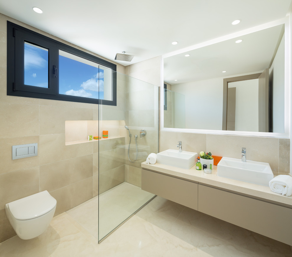 This is an example of a contemporary master bathroom in Other with beige cabinets, a curbless shower, beige tile, beige walls, a vessel sink, beige floor, beige benchtops, flat-panel cabinets and a wall-mount toilet.