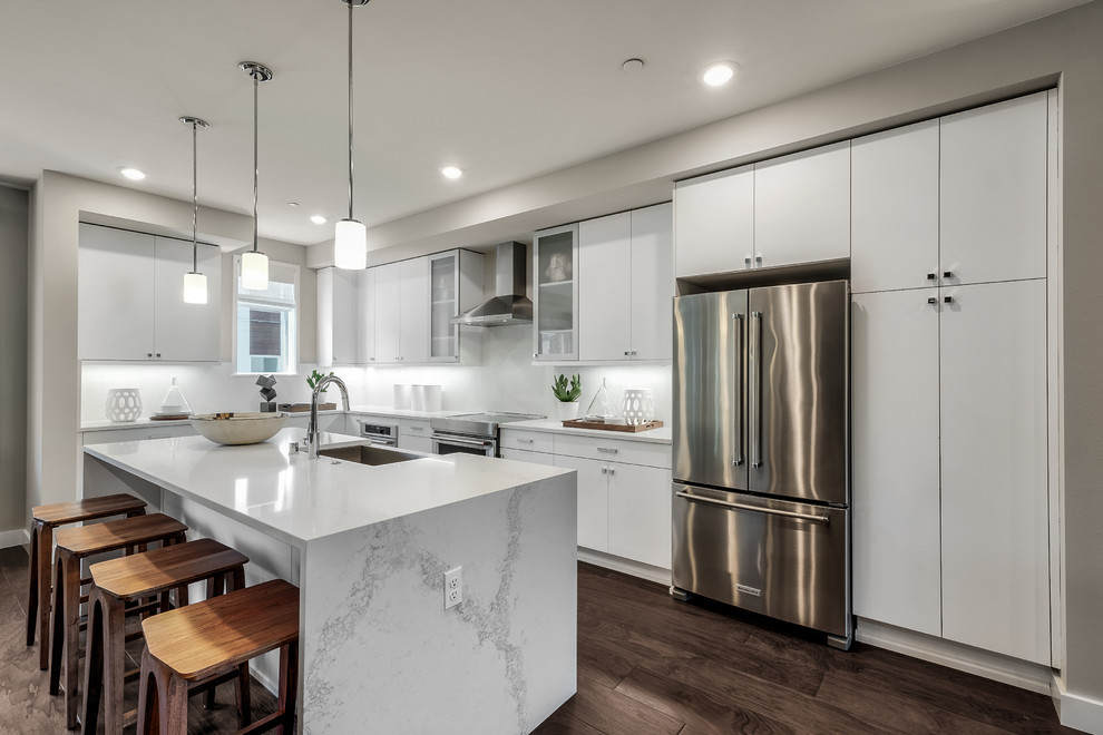 Inspiration for a modern l-shaped eat-in kitchen in Seattle with a farmhouse sink, flat-panel cabinets, white cabinets, quartz benchtops, white splashback, stainless steel appliances, medium hardwood floors, with island, brown floor and white benchtop.