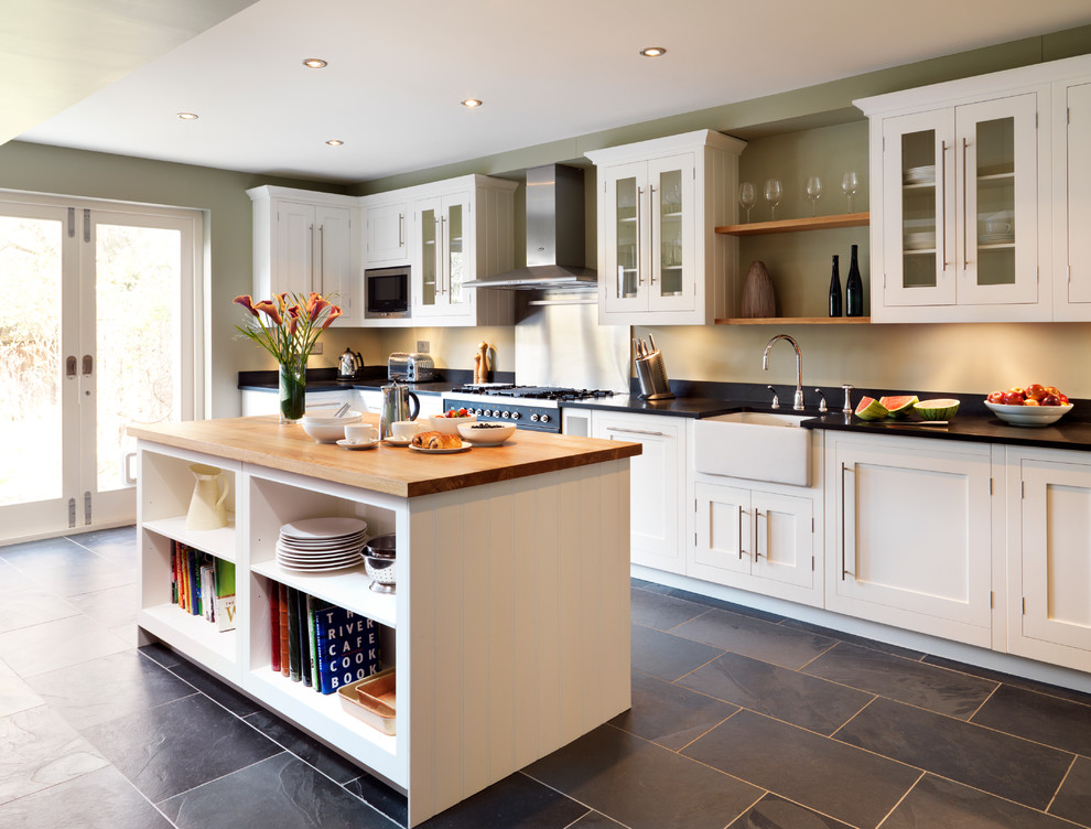 This is an example of a mid-sized traditional kitchen in London with a farmhouse sink, shaker cabinets, white cabinets, metallic splashback, slate floors and with island.