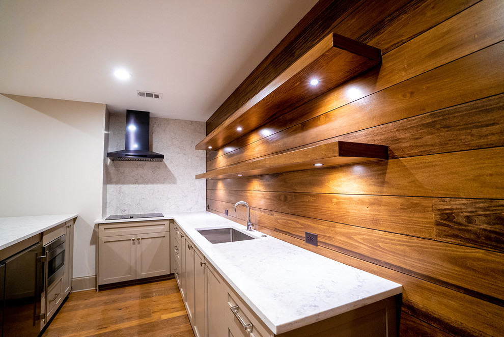 Photo of a mid-sized contemporary l-shaped seated home bar in Atlanta with an undermount sink, shaker cabinets, grey cabinets, quartz benchtops, brown splashback, timber splashback, medium hardwood floors, brown floor and white benchtop.