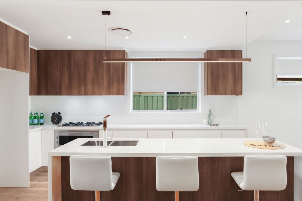 Inspiration for a large contemporary single-wall kitchen/diner in Sydney with a built-in sink, recessed-panel cabinets, medium wood cabinets, composite countertops, white splashback, marble splashback, stainless steel appliances, an island and white worktops.