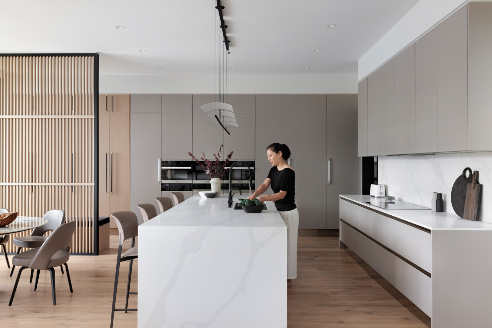 Photo of a modern eat-in kitchen in Vancouver with an undermount sink, flat-panel cabinets, grey cabinets, white splashback, light hardwood floors, with island and white benchtop.