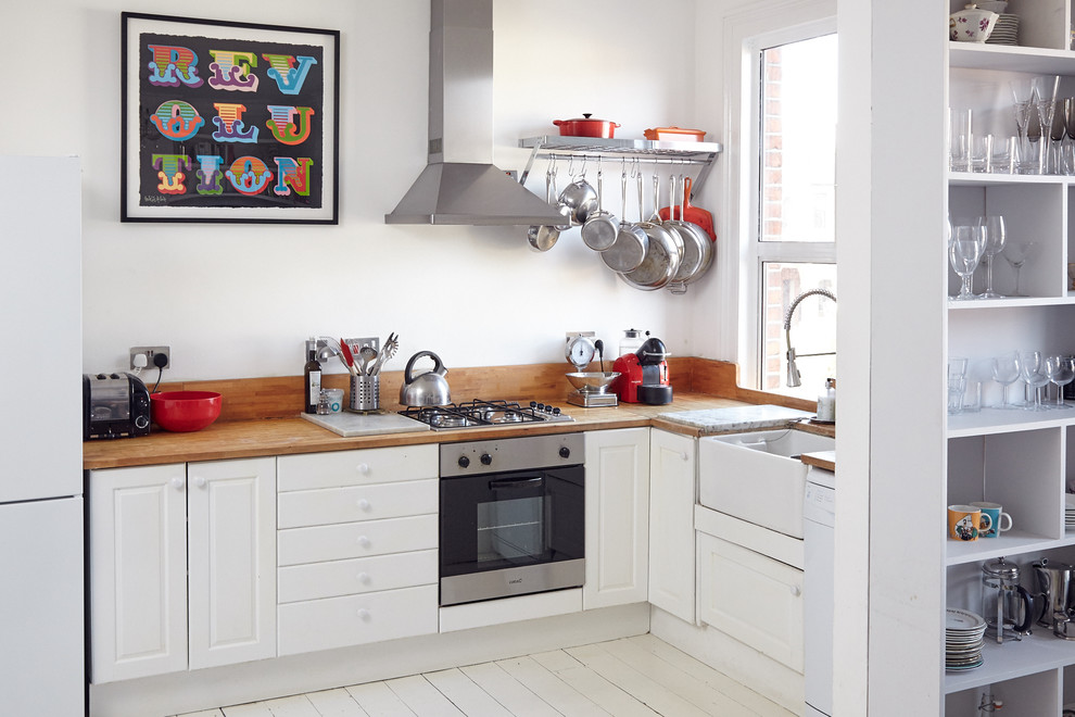 Photo of a small scandinavian l-shaped kitchen in London with a farmhouse sink, raised-panel cabinets, white cabinets, wood benchtops, painted wood floors and no island.