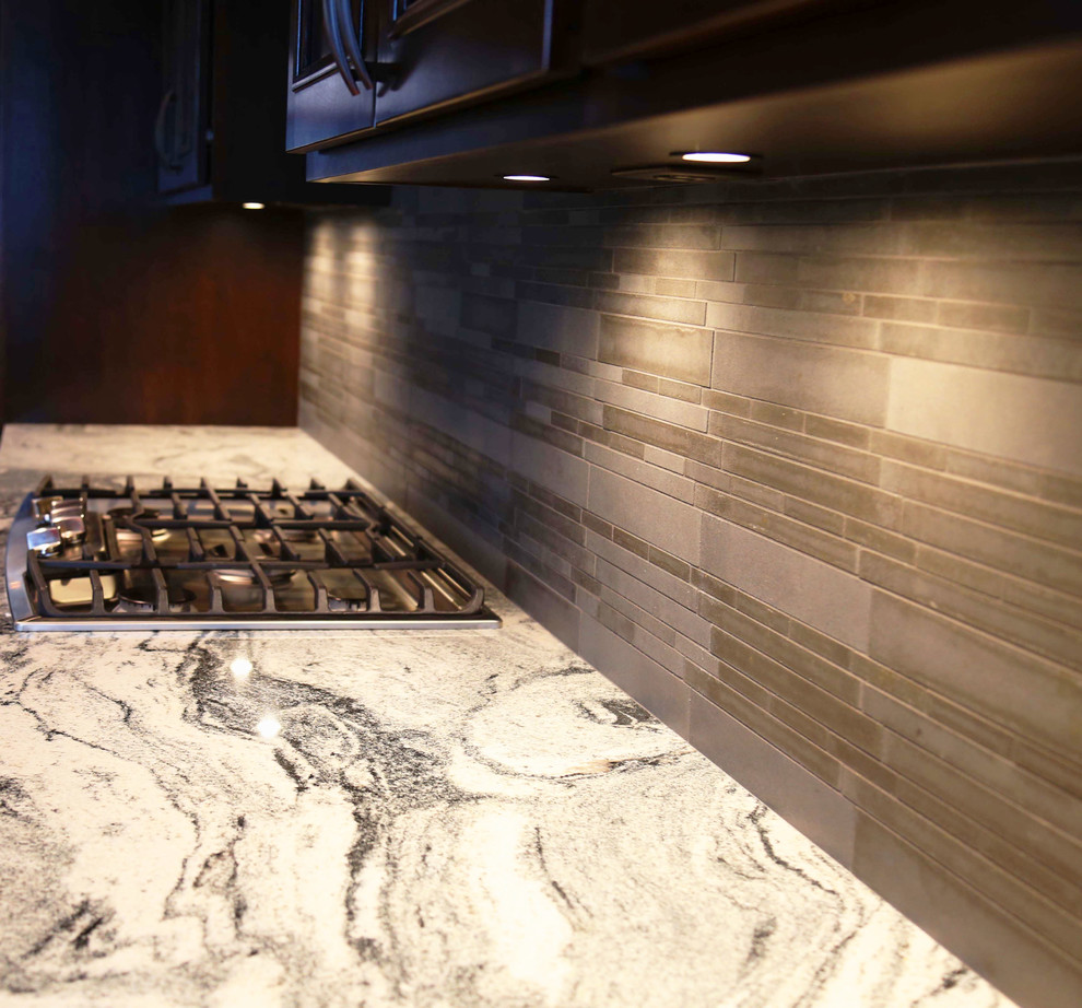 Example of a mid-sized transitional l-shaped porcelain tile eat-in kitchen design with an undermount sink, raised-panel cabinets, dark wood cabinets, granite countertops, gray backsplash, porcelain backsplash, stainless steel appliances and an island