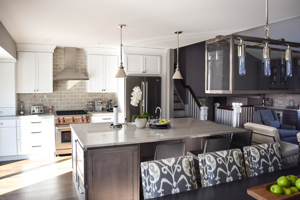 Mid-sized transitional single-wall eat-in kitchen in New York with a farmhouse sink, recessed-panel cabinets, white cabinets, quartzite benchtops, grey splashback, subway tile splashback, stainless steel appliances, dark hardwood floors and with island.