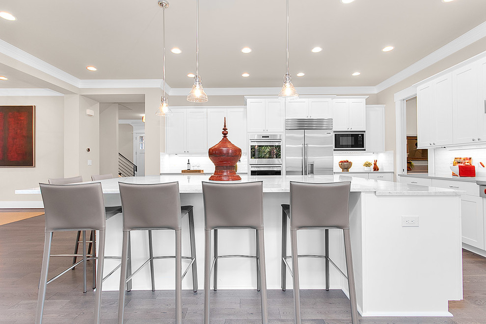 Design ideas for a large arts and crafts l-shaped eat-in kitchen in Seattle with recessed-panel cabinets, white cabinets, granite benchtops, white splashback, ceramic splashback, stainless steel appliances, medium hardwood floors and with island.