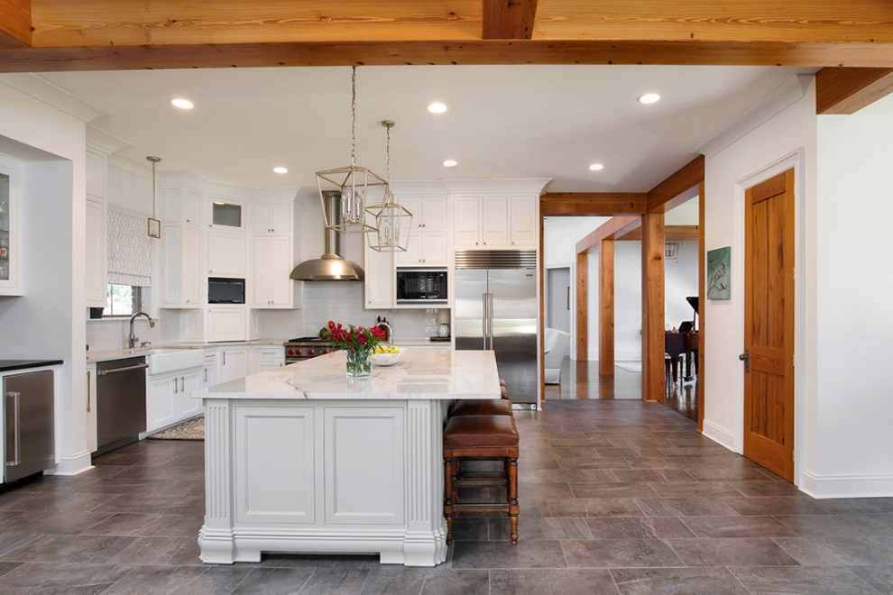 Inspiration for a mid-sized transitional l-shaped porcelain tile, gray floor and exposed beam eat-in kitchen remodel in New Orleans with a farmhouse sink, recessed-panel cabinets, white cabinets, quartzite countertops, gray backsplash, ceramic backsplash, stainless steel appliances, an island and white countertops