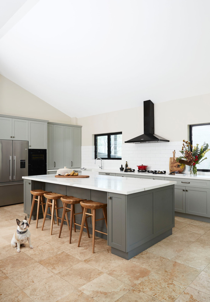 Photo of a large traditional l-shaped eat-in kitchen in Sydney with a farmhouse sink, shaker cabinets, green cabinets, quartz benchtops, white splashback, ceramic splashback, black appliances, travertine floors, with island, yellow floor and white benchtop.