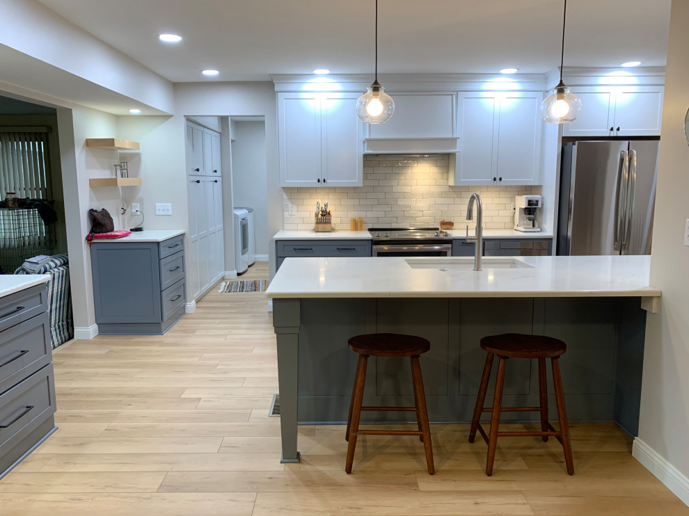 Example of a mid-sized classic galley open concept kitchen design in Other with an undermount sink, shaker cabinets, blue cabinets, quartz countertops, white backsplash, stainless steel appliances, an island and white countertops