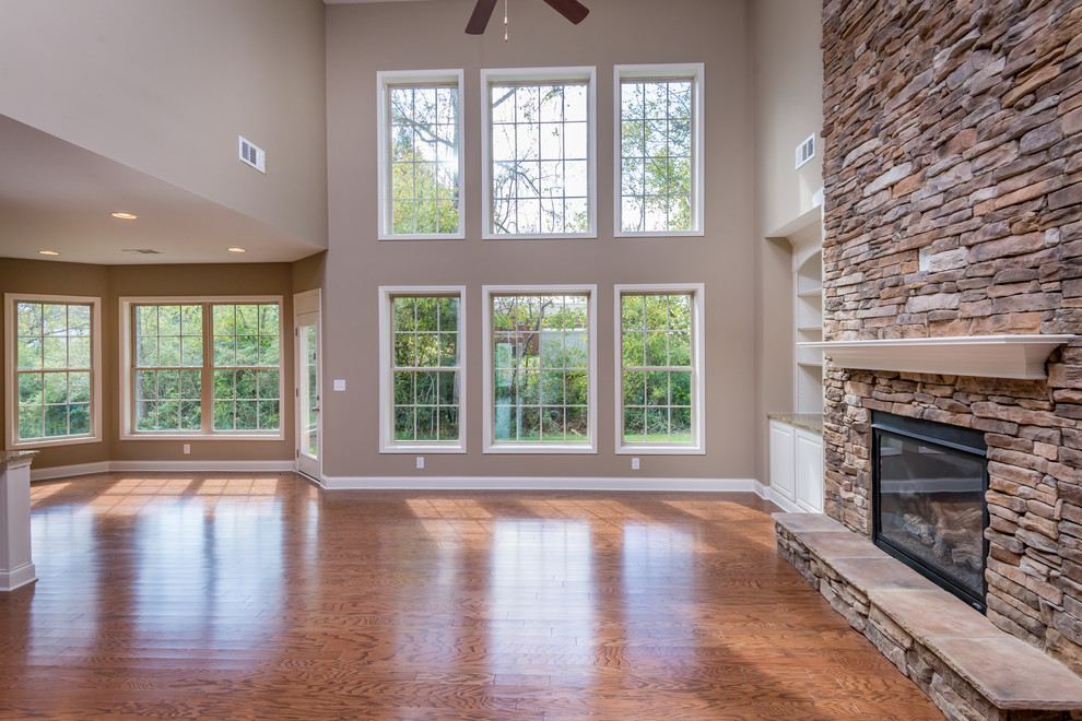 Example of a classic open concept medium tone wood floor family room design with beige walls, a standard fireplace and a stone fireplace
