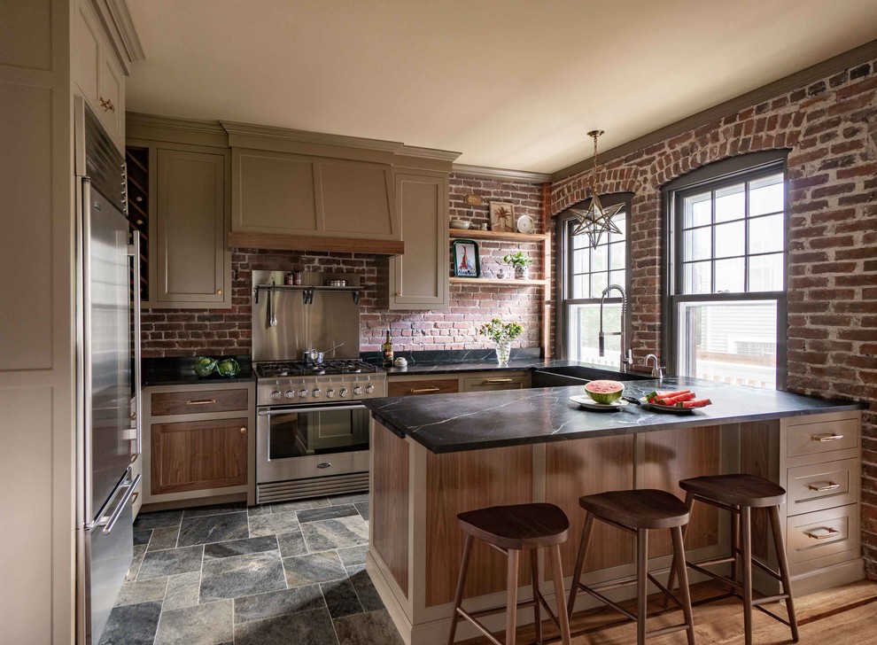 Inspiration for a country l-shaped kitchen in Boston with an undermount sink, shaker cabinets, brown cabinets, red splashback, brick splashback, stainless steel appliances, slate floors, with island, multi-coloured floor and black benchtop.
