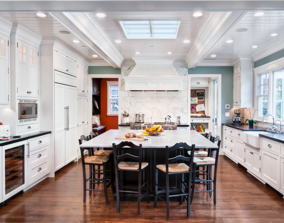 Inspiration for a traditional u-shaped eat-in kitchen in San Francisco with white cabinets, shaker cabinets, a farmhouse sink, medium hardwood floors, white splashback and panelled appliances.