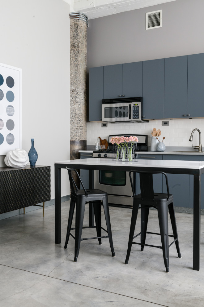 Small urban single-wall concrete floor, gray floor and exposed beam open concept kitchen photo in Minneapolis with a double-bowl sink, flat-panel cabinets, blue cabinets, white backsplash, ceramic backsplash, stainless steel appliances, an island, gray countertops and solid surface countertops