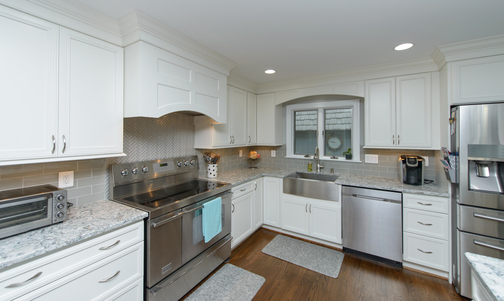 Example of a large transitional l-shaped dark wood floor and brown floor kitchen design in Baltimore with a farmhouse sink, recessed-panel cabinets, white cabinets, quartz countertops, gray backsplash, subway tile backsplash, stainless steel appliances and an island
