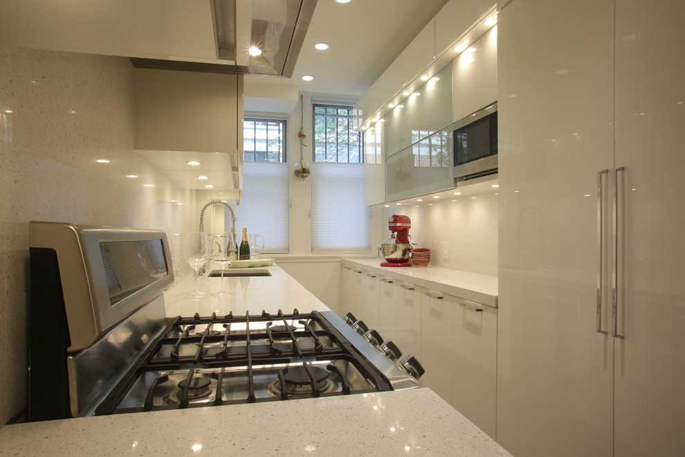 This is an example of a mid-sized modern galley separate kitchen in New York with an undermount sink, flat-panel cabinets, white cabinets, solid surface benchtops, multi-coloured splashback, stainless steel appliances, medium hardwood floors, no island and glass sheet splashback.