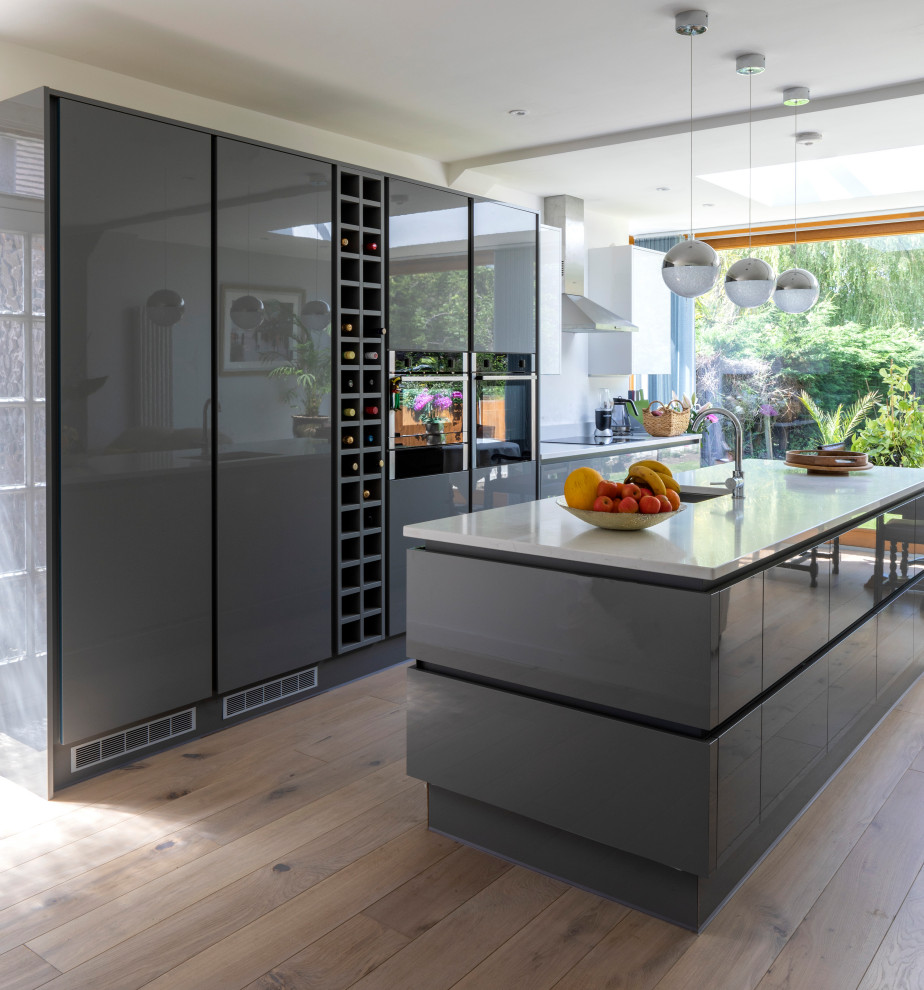 Inspiration for a mid-sized modern single-wall eat-in kitchen in London with an undermount sink, grey cabinets, quartzite benchtops, white splashback, stone slab splashback, panelled appliances, medium hardwood floors, with island and white benchtop.
