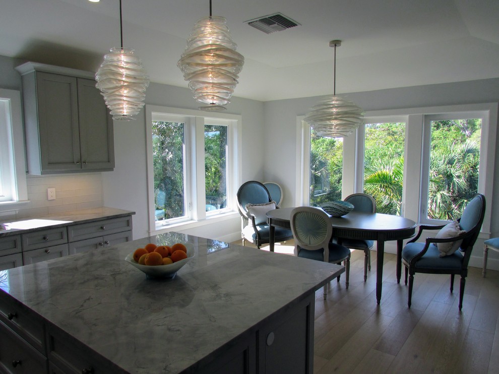This is an example of a mid-sized transitional l-shaped eat-in kitchen in Miami with an undermount sink, shaker cabinets, white cabinets, quartzite benchtops, white splashback, subway tile splashback, stainless steel appliances, light hardwood floors, with island and beige floor.