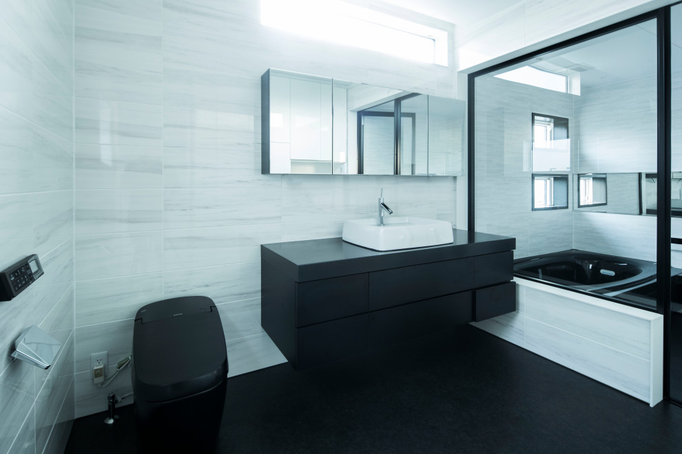 This is an example of a large modern powder room in Other with flat-panel cabinets, black cabinets, a one-piece toilet, white tile, mirror tile, white walls, vinyl floors, a vessel sink, solid surface benchtops, black floor, black benchtops, a floating vanity, wallpaper and wallpaper.