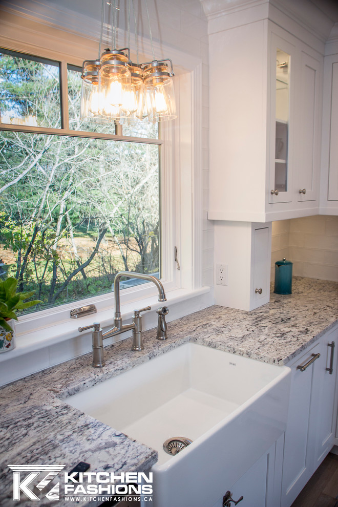 Large transitional u-shaped light wood floor home design photo with a farmhouse sink, shaker cabinets, white cabinets, granite countertops, white backsplash, subway tile backsplash, stainless steel appliances and no island