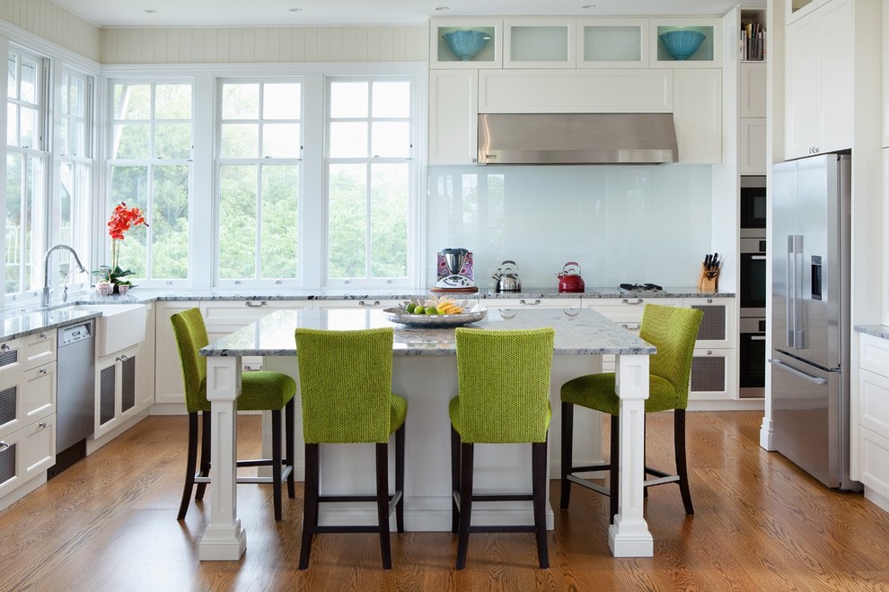 Photo of a transitional u-shaped kitchen in Brisbane with a farmhouse sink, recessed-panel cabinets, white cabinets, white splashback, glass sheet splashback, stainless steel appliances, medium hardwood floors and with island.
