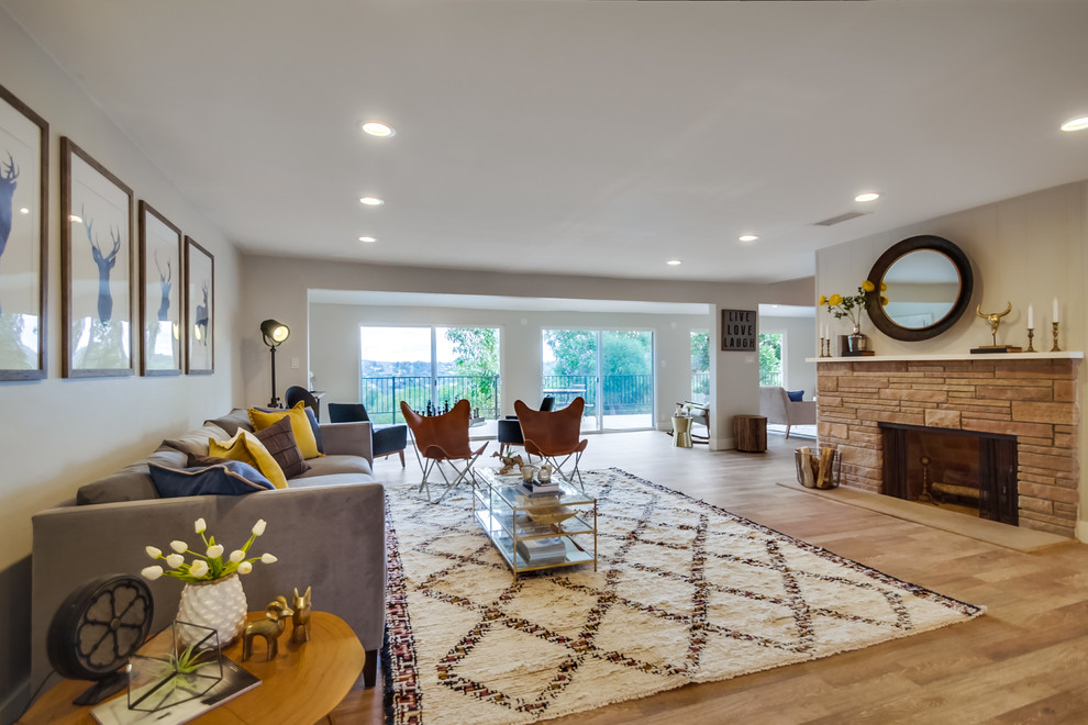 This is an example of a large eclectic open concept living room in San Diego with grey walls, light hardwood floors, a two-sided fireplace and a stone fireplace surround.
