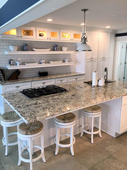 This is an example of a mid-sized beach style galley open plan kitchen in Other with an undermount sink, open cabinets, white cabinets, granite benchtops, white splashback, subway tile splashback, stainless steel appliances, ceramic floors, with island and beige floor.