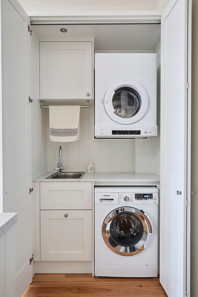 Inspiration for a mid-sized country laundry cupboard in Melbourne with shaker cabinets, white cabinets, marble benchtops, white splashback, porcelain splashback, a drop-in sink, white walls and medium hardwood floors.
