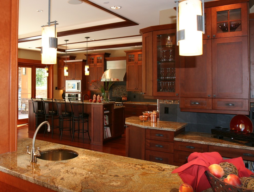 Photo of an arts and crafts l-shaped eat-in kitchen in Seattle with an undermount sink, recessed-panel cabinets, medium wood cabinets, granite benchtops, black splashback, stone tile splashback, stainless steel appliances, medium hardwood floors and multiple islands.