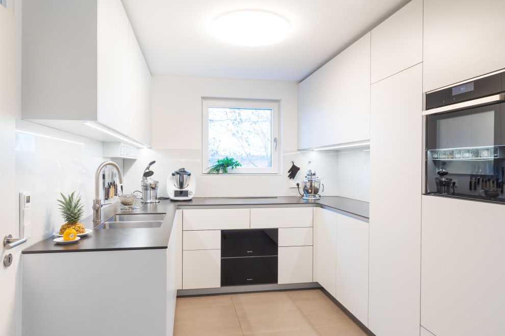 Geschlossene, Mittelgroße Klassische Küche in U-Form mit Doppelwaschbecken, weißen Schränken, schwarzen Elektrogeräten, grauem Boden, schwarzer Arbeitsplatte und Durchreiche in Stuttgart