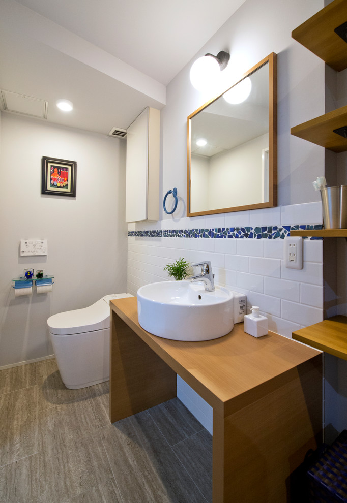 This is an example of an asian powder room in Yokohama with open cabinets, white tile, white walls, a vessel sink and grey floor.