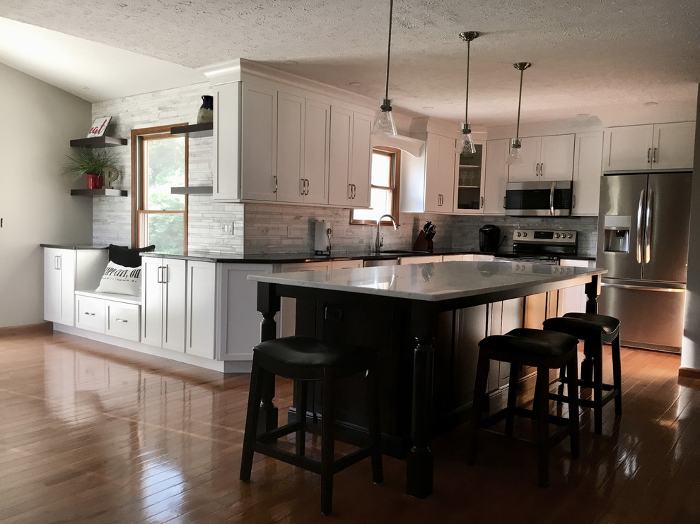 Example of a large transitional single-wall medium tone wood floor eat-in kitchen design with an undermount sink, shaker cabinets, white cabinets, granite countertops, multicolored backsplash, marble backsplash, stainless steel appliances, an island and black countertops