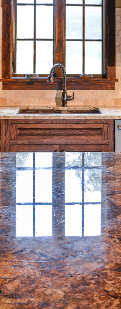 Example of a large mountain style l-shaped slate floor and gray floor enclosed kitchen design with an undermount sink, recessed-panel cabinets, dark wood cabinets, granite countertops, beige backsplash, stone tile backsplash, paneled appliances, a peninsula and brown countertops