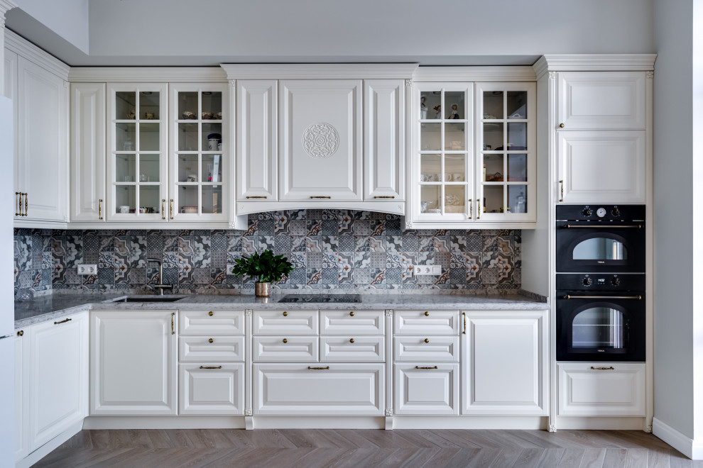 Eat-in kitchen - large traditional l-shaped porcelain tile and beige floor eat-in kitchen idea in Moscow with an undermount sink, raised-panel cabinets, white cabinets, quartz countertops, gray backsplash, ceramic backsplash, black appliances and gray countertops