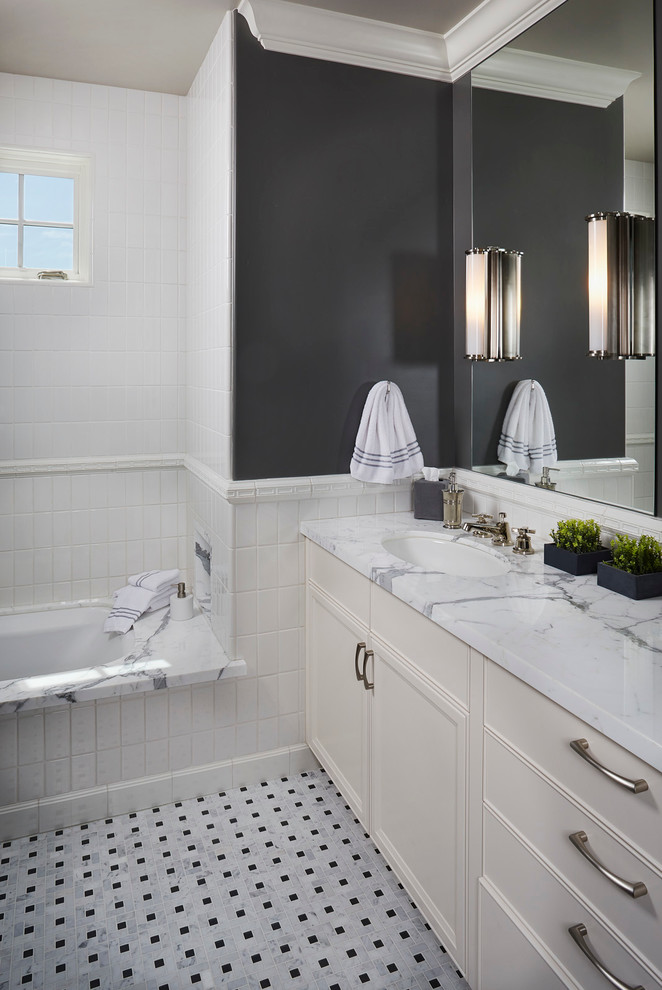 This is an example of a large traditional kids bathroom in San Francisco with raised-panel cabinets, beige cabinets, an undermount tub, a shower/bathtub combo, white tile, grey walls, mosaic tile floors, an undermount sink and marble benchtops.