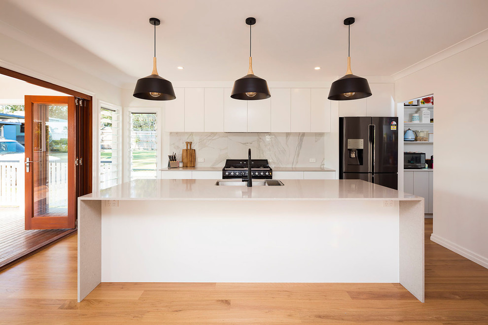 Design ideas for a small traditional galley open plan kitchen in Brisbane with an undermount sink, flat-panel cabinets, white cabinets, solid surface benchtops, white splashback, marble splashback, black appliances, light hardwood floors, with island and multi-coloured floor.