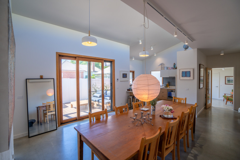 Aménagement d'une salle à manger ouverte sur la cuisine campagne de taille moyenne avec un mur blanc, sol en béton ciré et un sol gris.